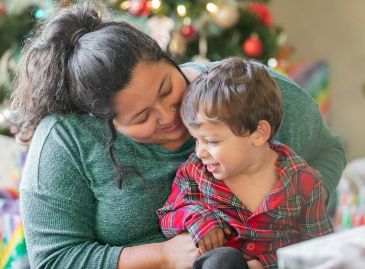 A mother and young son smiling together in front of holiday decorations