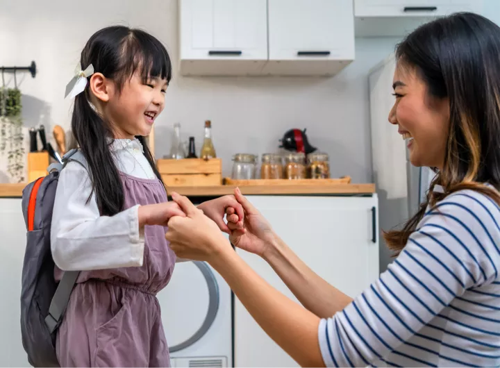 Mum and daughter looking happy and excited while getting ready for the childcare or school drop-off, showing a positive attitude through smiling and holding hands