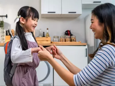 Mum and daughter looking happy and excited while getting ready for the childcare or school drop-off, showing a positive attitude through smiling and holding hands